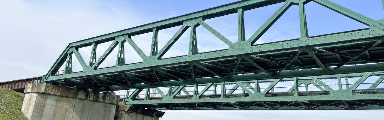 青空の下、河川に架けられた緑色のトラス型鉄道橋梁