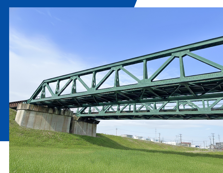 青空の下、河川に架けられた緑色のトラス型鉄道橋梁