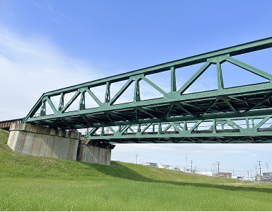 青空の下、河川に架けられた緑色のトラス型鉄道橋梁